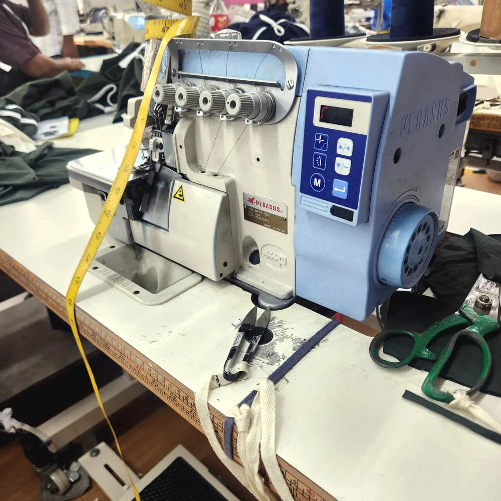 Overlock sewing station with garment panels in progress at a partner factory